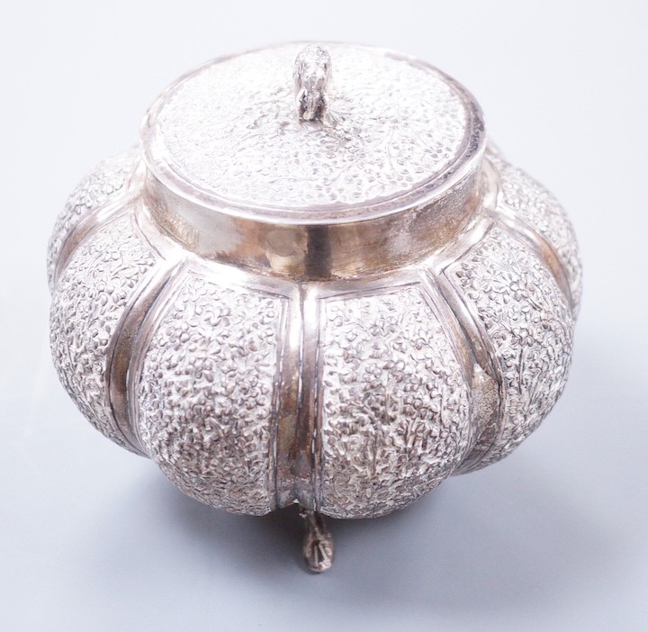 An Indian embossed lobed white metal circular pot and cover, with elephant finial, on three dolphin feet, height 10cm, 197 grams.